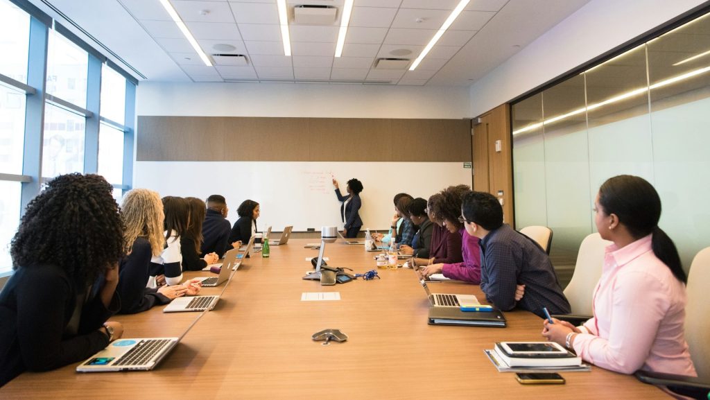 people on conference table looking at talking woman