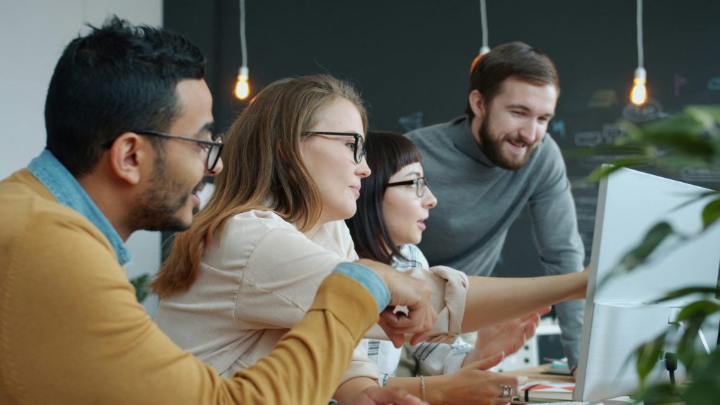 Diverse team collaborating around a computer screen.